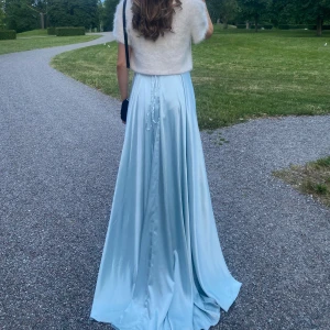 Ljusblå långklänning med v-ringning - Elegant ljusblå långklänning i satin med v-ringad hals och markerad midja. Klänningen har en mjuk, glansig yta och faller snyggt ner till golvet. Perfekt för bal eller fest. Bärs här med en vit kortärmad bolero. Har en knytning i ryggen som går att justera. För storlek, mått eller fler bilder kontakta mig här!🌸använd en gång. Nypris 3300 kr.