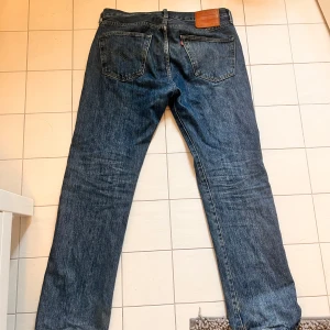 Levi's 501 jeans i blå denim - Klassiska blå Levi's 501 jeans med raka ben och femficksmodell. Byxorna har läderpatch bak i midjan och tydlig Levi's Premium-etikett på insidan. Ikonisk röd Levi's-tagg på bakfickan. Perfekta för en tidlös stil. Inga defekter, sparsamt använda, W33 L32