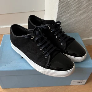 Lanvin toecap sneakers - Säljer ett par svarta Lanvin sneakers med snygg lackad tå och ovandel i mocka. Storlek uk 6 sitter 41-42 väldigt bra skick, sulkräm har använts så att sulorna ser ut som nya. Box och dustbaga ingår.