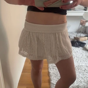 Vit spetskjol med bred resår - Supersöt vit kjol med bred resår i midjan och vacker spets över hela kjolen. Kjolen är kort och har en luftig känsla, perfekt för varma dagar. Passar till både enkla och mer uppklädda outfits.