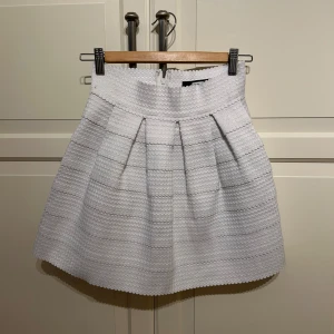 Vit kjol från Bik Bok - Säljer en söt vit kjol från Bik Bok i storlek S. Kjolen har en kort modell med veck framtill och ett diskret vågigt mönster i tyget. Perfekt för dig som gillar en stilren och fräsch look.