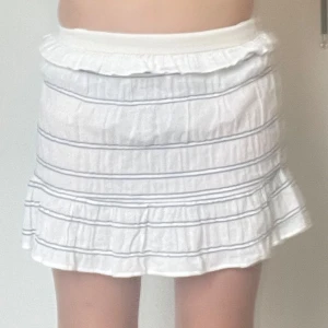 Vit volangkjol med blå ränder🩵💙 - Supersöt vit kjol med tunna blå ränder och volangkant upptill och nedtill.💗Kjolen har resår i midjan och är lätt utställd med en luftig känsla. Perfekt för varma dagar och enkel att styla med olika toppar.✨ storlek 146 men passar mig som har storlek 164!