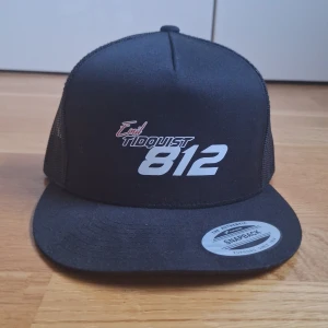 Svart snapback keps med tryck 'Emil Tidquist 812' - Svart snapback keps från Yupoong med vitt och rött tryck framtill: 'Emil Tidquist 812'. Kepsen har mesh baktill och justerbar passform. Klassisk rak skärm och ventilerande material.