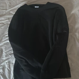 Svart sweatshirt från C.P. Company - Svart sweatshirt från C.P. Company med rund halsringning och en ficka med litet glaslinsmärke på ena ärmen. Klassisk och stilren modell i mjukt material, perfekt för en avslappnad look. Nypriss 2200. Kvitto finns och kommer med i frakten.