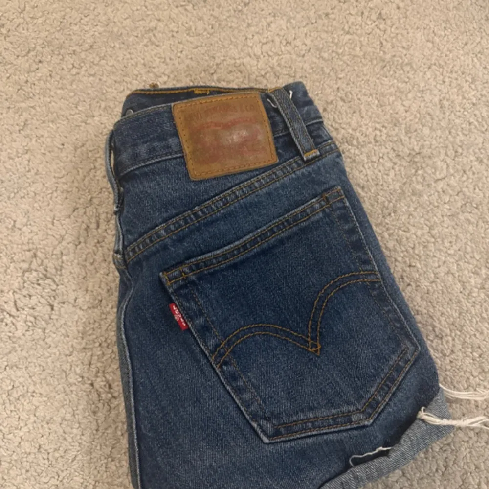Säljer ett par klassiska blå jeansshorts från Levi's med upprullade benslut och knappgylf. Shortsen har fem fickor och en läderpatch med logga på baksidan. Perfekta för en avslappnad stil.. Shortsit.