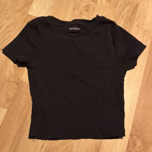 Svart ribbad topp från Even&Odd - Säljer en svart ribbad, croppad topp från Even&Odd. Den har en enkel design med korta ärmar och rund hals. Perfekt för en stilren look.