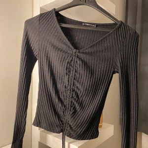 Svart ribbad topp  - Snygg svart ribbad topp med v-ringning och snörning framtill. Perfekt för en stilren look. Långärmad och figurnära passform som framhäver silhuetten. Storleken är xxs men kan töjs ut till xs eller s. Använd men i fint skick, lite nopprig bara.