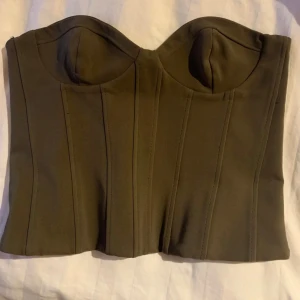 Olivgrön korsett - Snygg olivgrön korsett med en strukturerad design och formade kupor. Perfekt för att ge en stilren och elegant look. Passar bra till både jeans och kjol för en chic outfit.