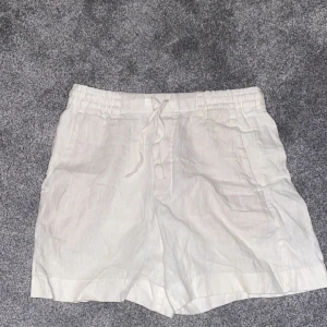 Vita linneshorts med snörning - Snygga och bekväma vita shorts i linne med elastisk midja och snörning. Perfekta för varma dagar med en avslappnad stil. De har en bakficka för extra funktionalitet. Ser nya ut om man stryker dem