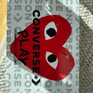 CDG Play X Converse Skor - Säljer ett par svarta Converse x Comme des Garçons Play sneakers med det ikoniska röda hjärtat på sidan. Skorna har vita snören och en klassisk vit sula. Perfekta för dig som vill ha en stilren och trendig look.