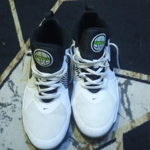 Vita och svarta Nike sneakers - Snygga vita och svarta Nike sneakers med coola mönster på sidorna och en grön detalj på sulan. Skorna har snörning och en tydlig Nike-logga på sidan. Perfekta för en sportig look.