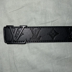 Svart bälte sjuk kvalité  - Snyggt svart bälte med präglad logotyp och monogramdetaljer. Bältet har ett stilrent spänne med logotypen i svart metall. Perfekt för att ge en lyxig touch till din outfit. Detta bälte är helt nytt och har används 2 gånger.