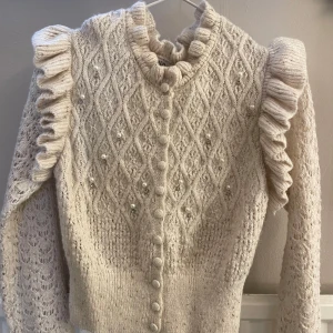 Beige stickad kofta från Zara - Säljer en söt beige stickad kofta från Zara med vackra volangdetaljer längs ärmarna och knappar framtill. Koftan har ett fint mönster och pärldetaljer, storlek M men passar även S. 🤍