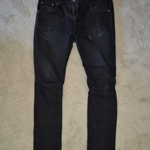 Svarta jeans från Nudie Jeans - Snygga svarta jeans från Nudie Jeans med en stilren design. De har en klassisk femficksmodell och en knappgylf. Perfekta för en stilren look. Modellen Lean Dean. Storlek W30L30.