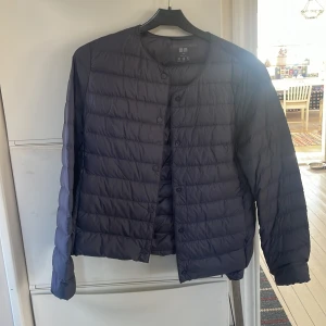 Mörkblå dunjacka från Uniqlo - Säljer en mörkblå/lila ultralätt dunjacka från Uniqlo. Jackan har en stilren design med knappar framtill och är perfekt för lager-på-lager. Den är långärmad och quiltad, vilket ger extra värme utan att kännas tung. Perfekt för våren! Köpt för:899kr obs! Aldrig använd så den är som ny!pris kan diskuteras vid snabb försäljning.