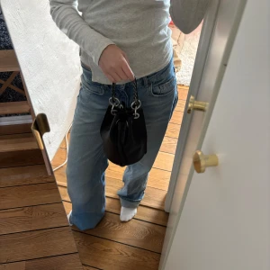 Svart väska med nitar - Snygg svart växa med coola nitar på handtaget. Väskan har en unik design med stora metallringar och snörning upptill. Perfekt för att ge din outfit en edgy touch.