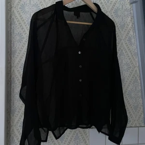 Svart transparent blus - Snygg svart transparent blus med knappar framtill. Krage och två bröstfickor. Står ej storlek men skulle säga S/M