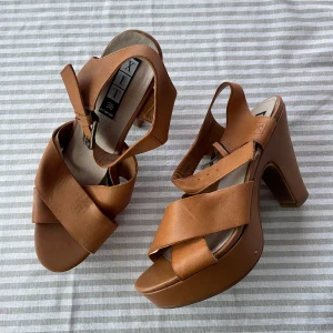 Bruna klackskor - Bruna klackar med breda remmar och en stabil klack. Behöver limmas lite då fodret börjar lossna från ”lädret”. Någon liten repa i sulan/klackan