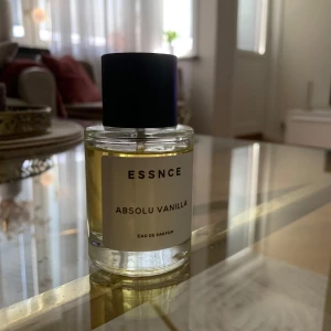 Essnce Absolu Vanilla Eau de Parfum - Säljer en flaska Essnce Absolu Vanilla Eau de Parfum. Doften har en varm och söt vaniljton. Flaskan är genomskinlig med en svart kork och en enkel, stilren etikett.