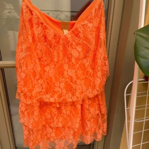Korall spetsklänning - Säljer en ärmlös korall klänning med vacker spetsdetalj. Perfekt till sommaren med sin livfulla färg och eleganta design. Klänningen har en omlott-look och är ärmlös. 