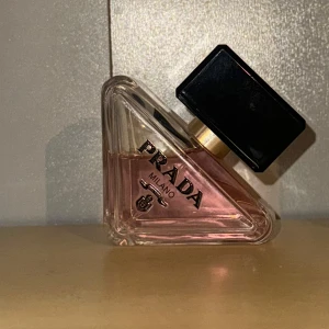 Prada Milano parfym - Elegant parfym från Prada i en unik triangulär flaska med rosa doftvätska. Flaskan har en svart fyrkantig kork och guldiga detaljer. Parfymen har används VÄLDIGT sparsamt! (30ml)