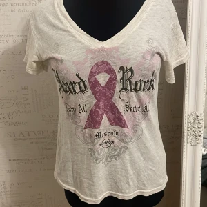 t-shirt Hard Rock Cafe - Säljer en vit t-shirt från Hard Rock Cafe med ett stort tryck i rosa och svart på framsidan. T-shirten har en v-ringad hals och är kortärmad. Perfekt för en avslappnad stil. Passar M och S jättefin y2k 2000s