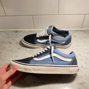 Blå och svarta sneakers från Vans - Snygga Vans sneakers i en kombination av mörkblått och ljusblått med vita detaljer. Skorna har klassisk snörning och en vit sula med det ikoniska våffelmönstret undertill. Perfekta för en avslappnad stil.