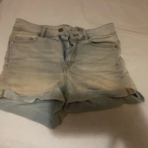 Ljusblå jeansshorts - Säljer ett par jeansshorts med upprullade ben och klassisk urtvättad stil. Shortsen har en knapp och dragkedja framtill. Perfekta för en avslappnad look inför sommaren😍.