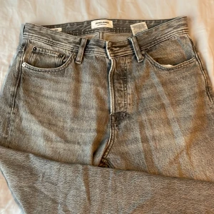 Grå jeans från Jack & Jones - Snygga grå jeans från Jack & Jones i modellen Relaxed/Chris. De har en avslappnad passform med klassisk femficksdesign och knappgylf. Perfekta för en casual look.