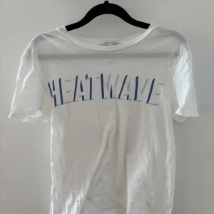 Vit t-shirt från Joelle med tryck - Säljer en vit t-shirt från Joelle med blått tryck 'HEATWAVE' på framsidan. T-shirten har en klassisk rund hals och korta ärmar. 