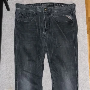 Svarta jeansbyxor från Replay - Snygga svarta jeansbyxor från Replay i modellen Anbass. De har en klassisk femficksdesign med knapp och dragkedja framtill. Perfekta för en stilren look.