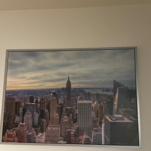 Tavla med New Yorks skyline - Stor tavla som visar New Yorks ikoniska skyline med Empire State Building i centrum. Perfekt för att ge rummet en urban känsla och påminna om storstadens puls. Tavlan har en stilren ram som kompletterar motivet.