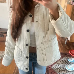 Vit quiltad jacka från Zara - Säljer en snygg vit quiltad jacka från Zara med svarta knappar. Jackan har en croppad passform och långa ärmar. Perfekt för en stilren look.