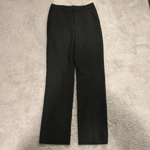 Svarta kostymbyxor från Lindex - Snygga svarta kostymbyxor från Lindex med en klassisk rak passform. Perfekta för en stilren look. Byxorna har en diskret dragkedja och knapp framtill.