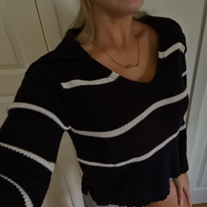 Svartvitrandig stickad tröja - Snygg svart stickad tröja med vita ränder och bred, ribbstickad krage. Tröjan har v-ringning, långa ärmar med en slits längst ner. Super mjuk och skön i materialet, perfekt nu inför kommande höst! Styla med en stickad kjol, oversized jacka eller kappa med ett par boots eller höga stövlar! (Nypris 599)