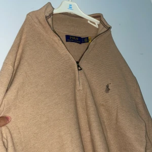 Beige stickad half zip från Polo Ralph Lauren - Säljer en beige stickad tröja från Polo Ralph Lauren med half zip och broderad logga på bröstet. Tröjan har lång ärm, ribbade muddar och hög krage. Perfekt för lager-på-lager och chill stil. Köpt från polo butik för 2500 kr, samt använt tröjan en gång!