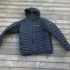 Svart dunjacka Peak Performance XL - Säljer en svart dunjacka från Peak Performance i storlek XL. Jackan har huva, dragkedja framtill och quiltad design med horisontella sömmar. Perfekt för kyliga dagar och enkel att matcha med olika outfits. Den har ett litet märkte på sig som man kan se i sista bilden