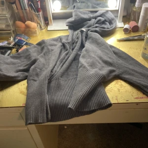 Mörkgrå hoodie från Ginatrigo - Mysig mörkgrå hoodie från Ginatrigo med dragkedja framtill och breda ribbade muddar vid ärmslut och nederkant. Tröjan har huva och är långärmad, perfekt för kyliga dagar. Materialet känns mjukt och skönt mot huden.