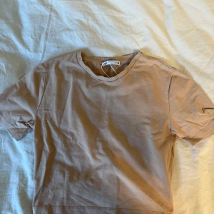 Beige t-shirt från zara - Snygg beige t-shirt från zara med klassisk rund hals och korta ärmar. Modellen är enkel och stilren, perfekt för dig som gillar minimalistisk look. Tillverkad i mjuk bomull som känns skön mot huden. Passformen är normal och t-shirten är lätt att matcha med allt.