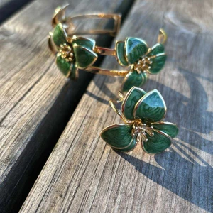 Grönt blommigt armband och ring - Säljer ett set med armband och ring i guldton med stora gröna blommor. Blommorna har detaljerade blad och guldfärgade pistiller i mitten, vilket ger en lyxig och unik känsla. Perfekt för dig som vill sticka ut med coola accessoarer.
