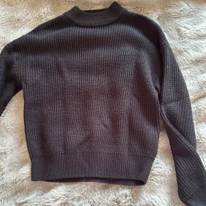 Svart stickad tröja  - Säljer en svart stickad polotröja med ribbad struktur och hög hals. Tröjan har långärmade och en klassisk, lite loose passform som är perfekt för kyliga dagar. Enkel och stilren design som funkar till många olika outfits.