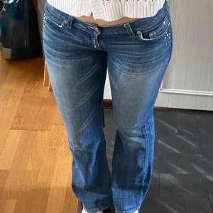 Blå bootcut jeans med strassdetaljer - Snygga blå bootcut jeans från Divided by H&M med coola strassdetaljer på bakfickorna. Finns vissa tecken på användning, men har fortfarande såå mycket kvar att ge!! Perfekta för dig som gillar lite extra bling på dina byxor. Midjemått: 36cm, Innerbenslängd: 75cm