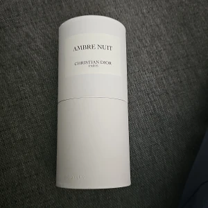 Ambre Nuit parfym från Dior 125ml - Ambre Nuit Eau de Parfum från Christian Dior i en stilren, cylindrisk glasflaska med svart lock och vit etikett. Parfymen är bärnstensfärgad och kommer i en elegant vit kartong. Flaskan rymmer 125 ml och har en lyxig känsla, perfekt för dig som gillar exklusiva dofter.