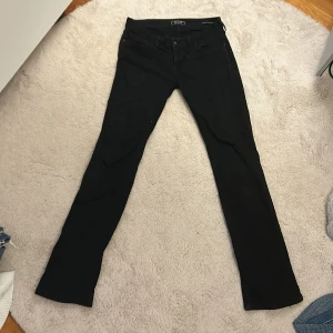 Svarta straight jeans från Guess - Svarta jeans från Guess med klassisk femficksdesign och snygga detaljer på bakfickorna. Modellen är straight fit/ bootcut och har diskreta svarta nitar och knapp med Guess-logga. Materialet är mjukt och stretchigt för extra komfort. 