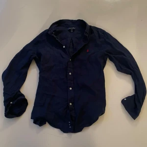 Polo Ralph lauren  - Säljer en klassisk mörkblå skjorta från Polo Ralph Lauren i storlek kids XL 18-20 men skulle säga att den sitter som S. Skjortan har långa ärmar, knappar framtill och den ikoniska röda loggan broderad på bröstet. Perfekt för dig som gillar stilrena och tidlösa plagg.