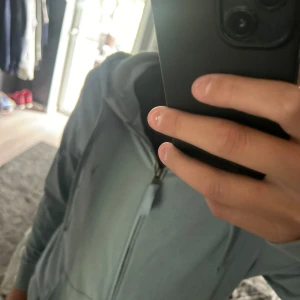 Grå blå zip-hoodie från AllSaints - Säljer en grå blå hoodie med dragkedja från AllSaints i 100% ekologisk bomull. Jackan har huva, långa ärmar och en broderad logga på bröstet. Perfekt för chill dagar och enkel att matcha med jeans eller joggers.