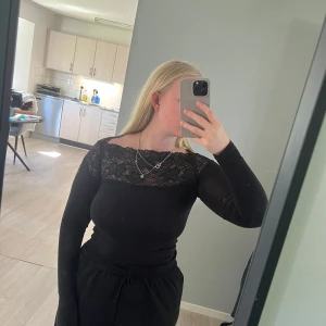 Svart topp med spetsdetalj - Svart långärmad topp med spets upptill över bröst och axlar. Storlek xs från Kappahl 