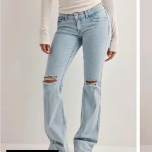 Ljusblå bootcut jeans med slitningar - Säljer ett par ljusblå bootcut jeans med slitna knän och broderade detaljer på bakfickorna. Jeansen har klassisk femficksdesign och är tillverkade i mjukt denimtyg. Perfekta för dig som gillar en avslappnad och trendig look. Knappast använda 