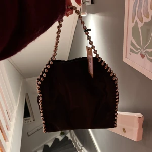Svart axelväska med pärldetaljer - Säljer en svart axelväska i NY SKICK med coola pärldetaljer längs kanterna och handtaget. 