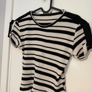 Randig stickad topp från Zara - Snygg stickad topp från Zara i svart och vitt med horisontella ränder. Modellen har korta ärmar med knytband på axlarna och en ribbad struktur (det ska vara så). Tröjan är i storlek S men skulle säga att den även passar dig som bär XS. Använt några få gånger.